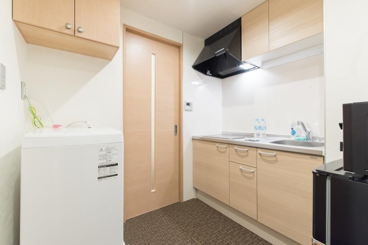A compact kitchen with a refrigerator, stove, sink, and black range hood.