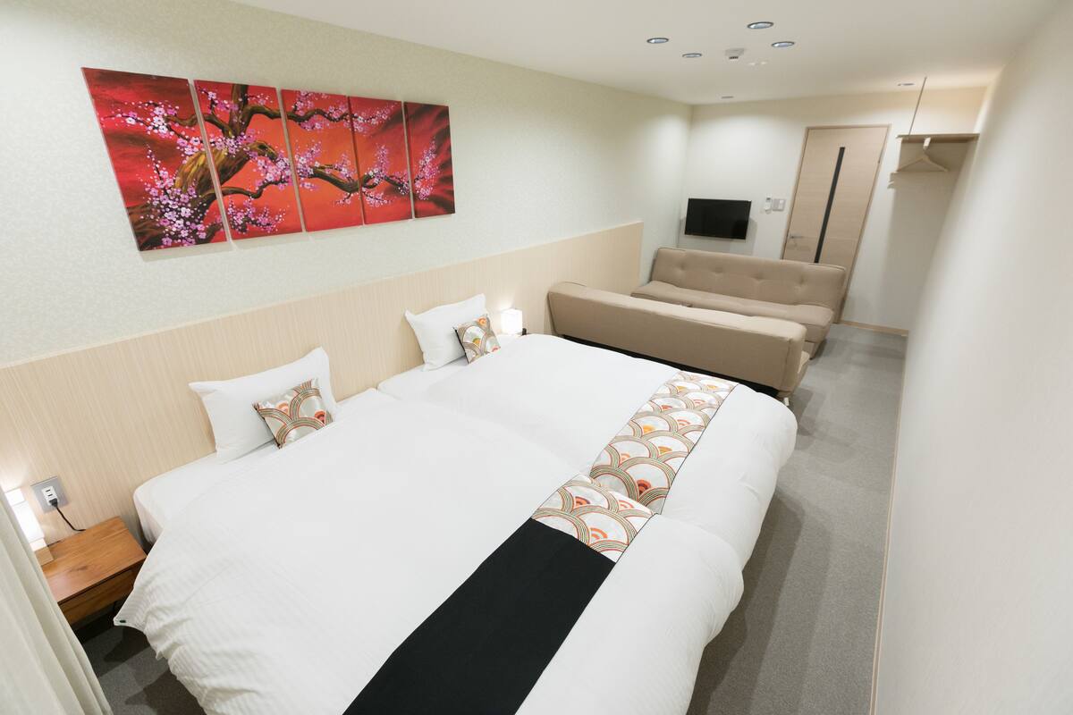 A hotel room with a large bed, a sofa, a TV, and a painting on the wall.