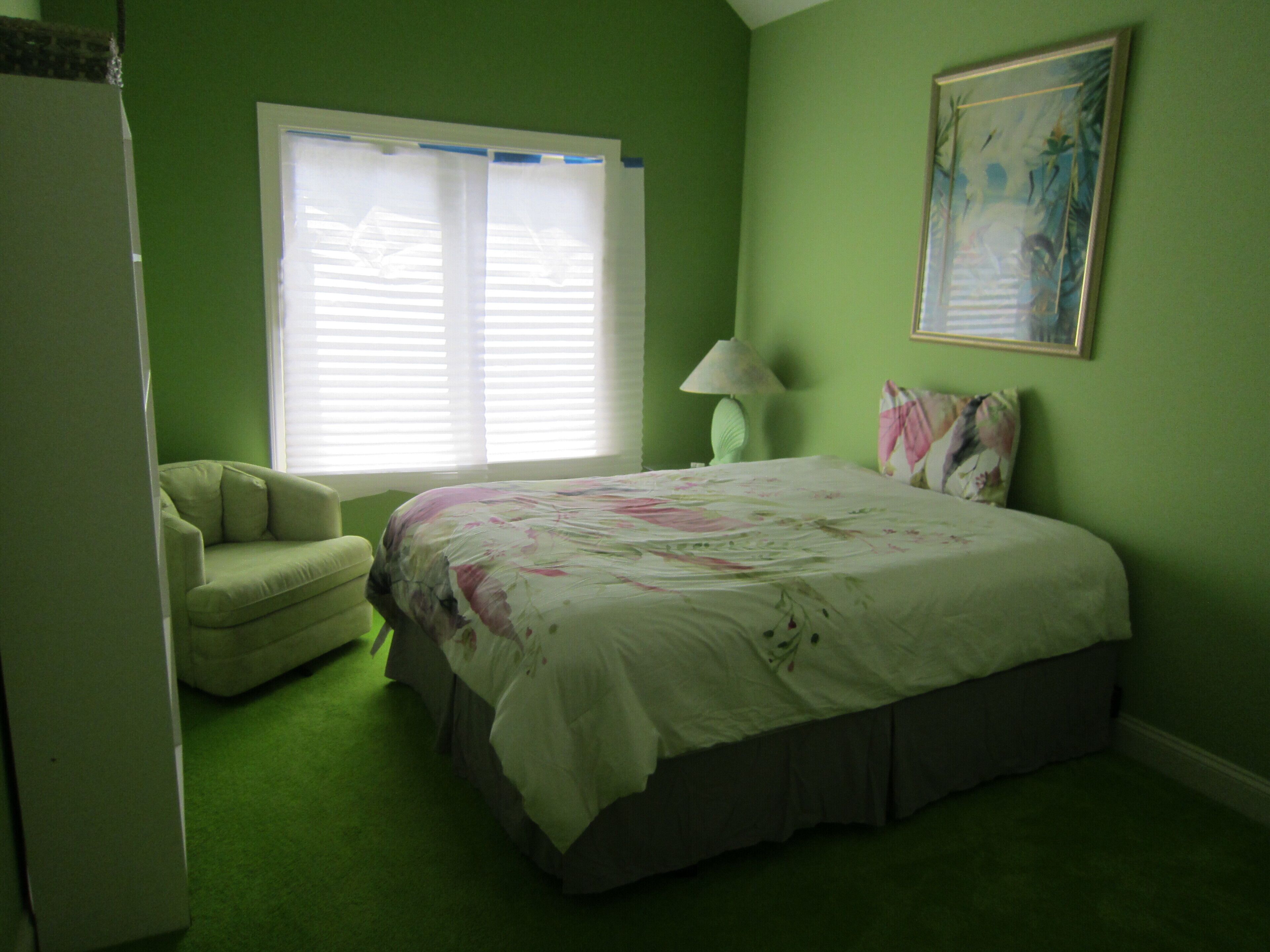 A bedroom with a bed, a chair, a nightstand, a lamp, and a window with blinds.