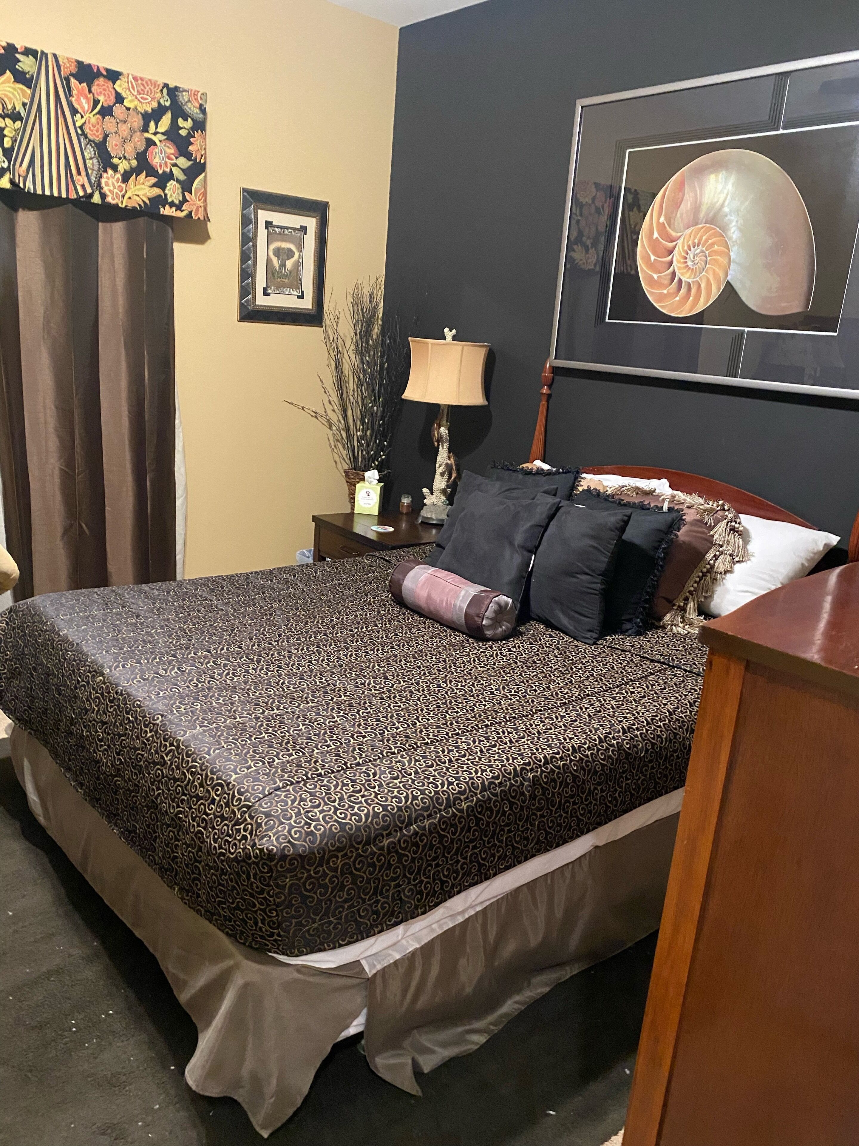 A neatly made bed with patterned bedding, a bedside lamp, a framed picture, and a decorative wall hanging.