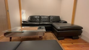 A living room with a black leather sofa, a glass coffee table, and a wooden floor. - Kamo-Zen (Kyoto)