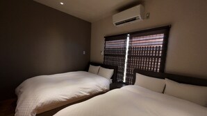 A hotel room with two single beds, a window with blinds, an air conditioning unit, and a wooden floor. - Kamo-Zen (Kyoto)