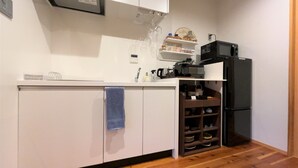 A compact kitchen with white cabinets, a black refrigerator, and wooden flooring. - Kamo-Zen (Kyoto)