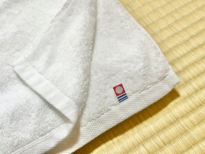 A white towel with a small embroidered tag on a textured surface. - Kamo-Zen (Kyoto)