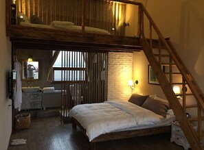 Camera da letto con letto a soppalco, scala in legno, piccolo bagno con specchio e finestra con tende.