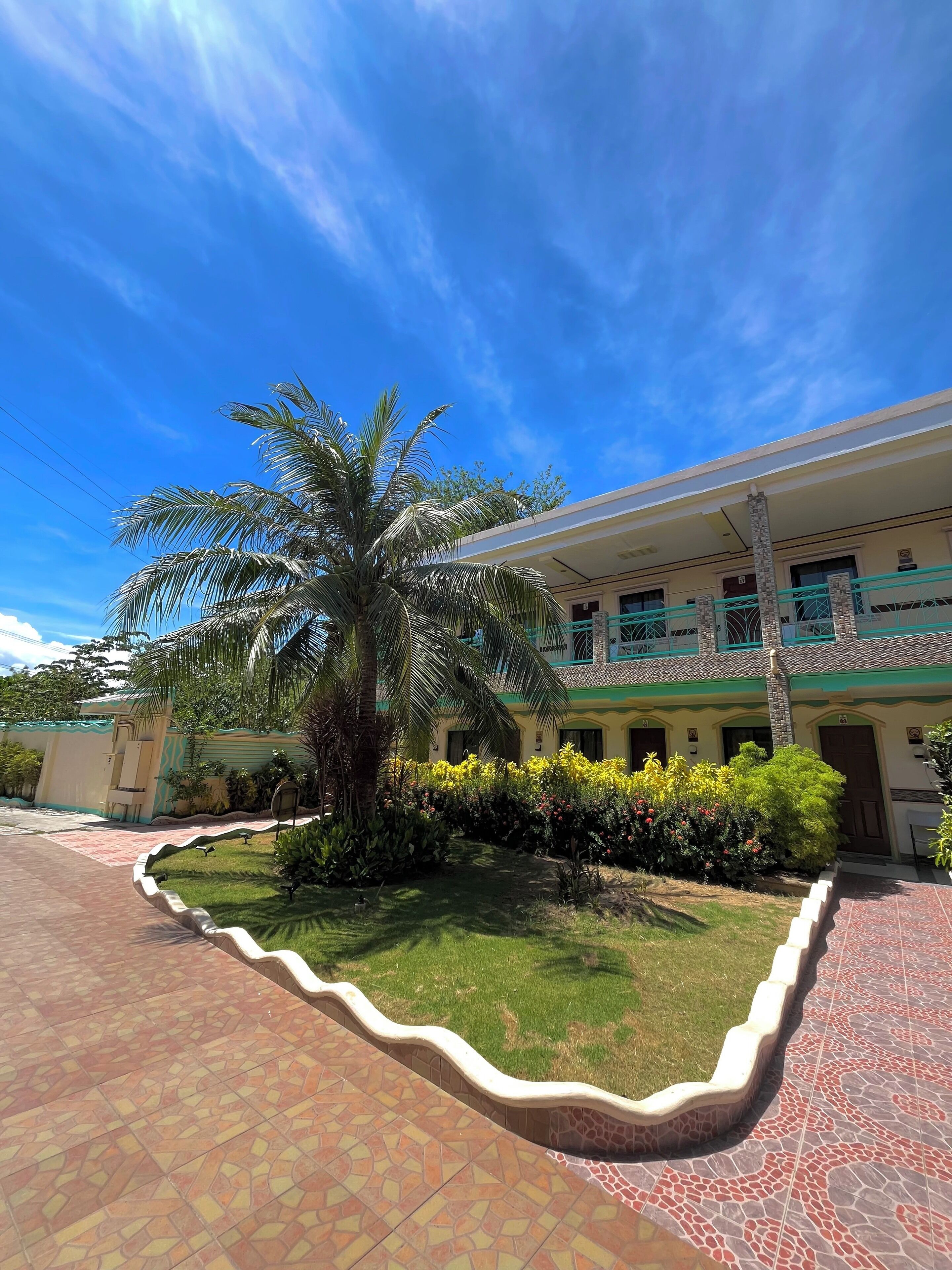 A building with a tiled patio, a palm tree, and a well-maintained garden.