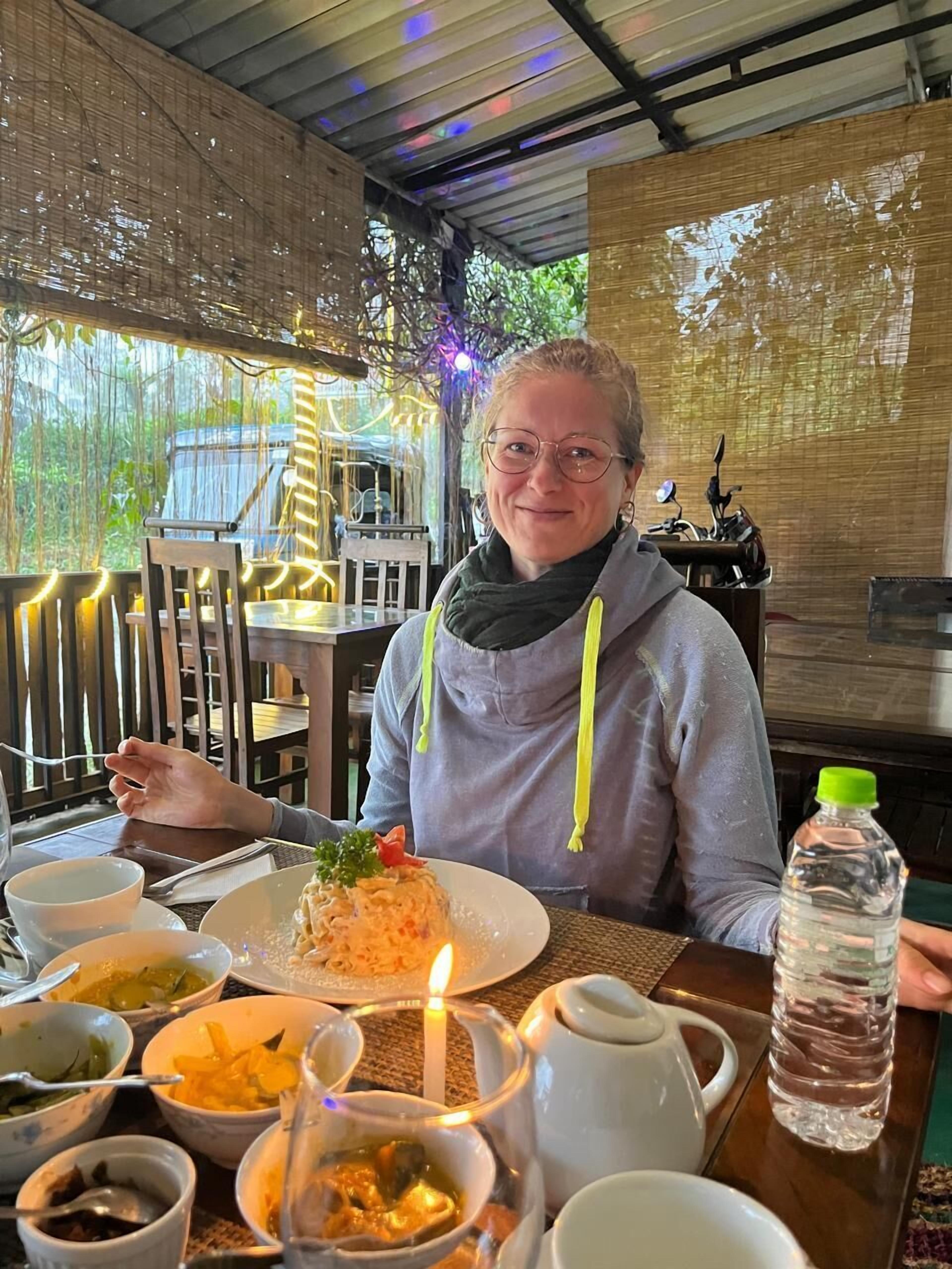 A person seated at a table with various dishes, a candle, and a water bottle.