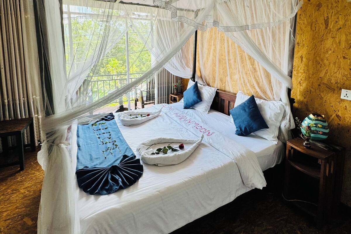 A bed with a canopy, a bedside table, and a view of greenery outside.