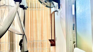 A room with a bed, a standing fan, a door, and a curtain.