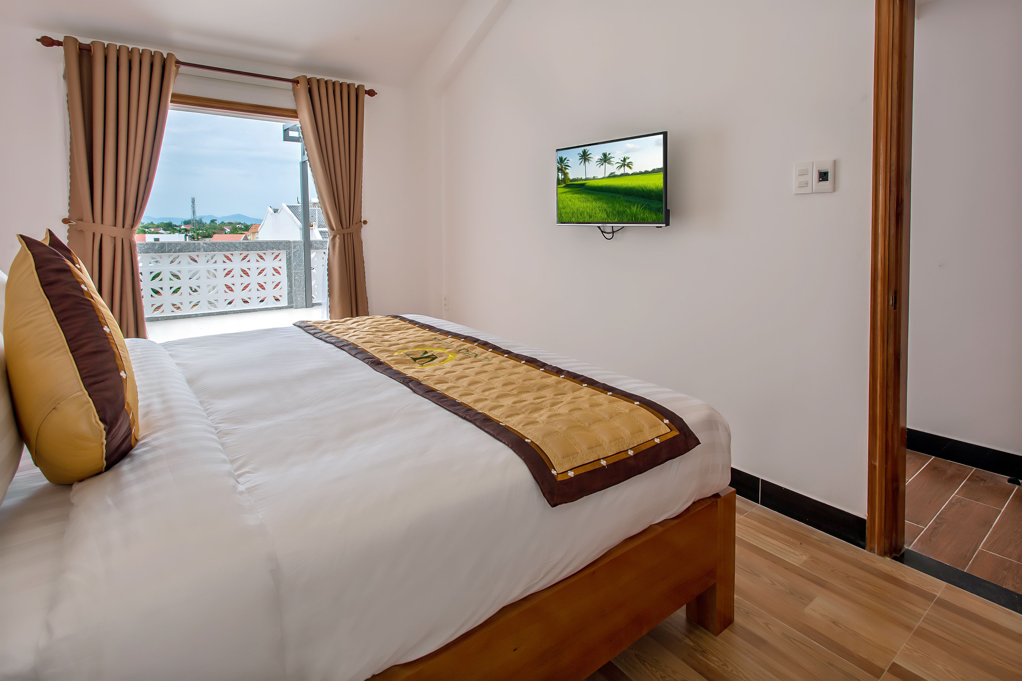 Un dormitorio con cama, cortinas, televisor en la pared y vistas al balcón.