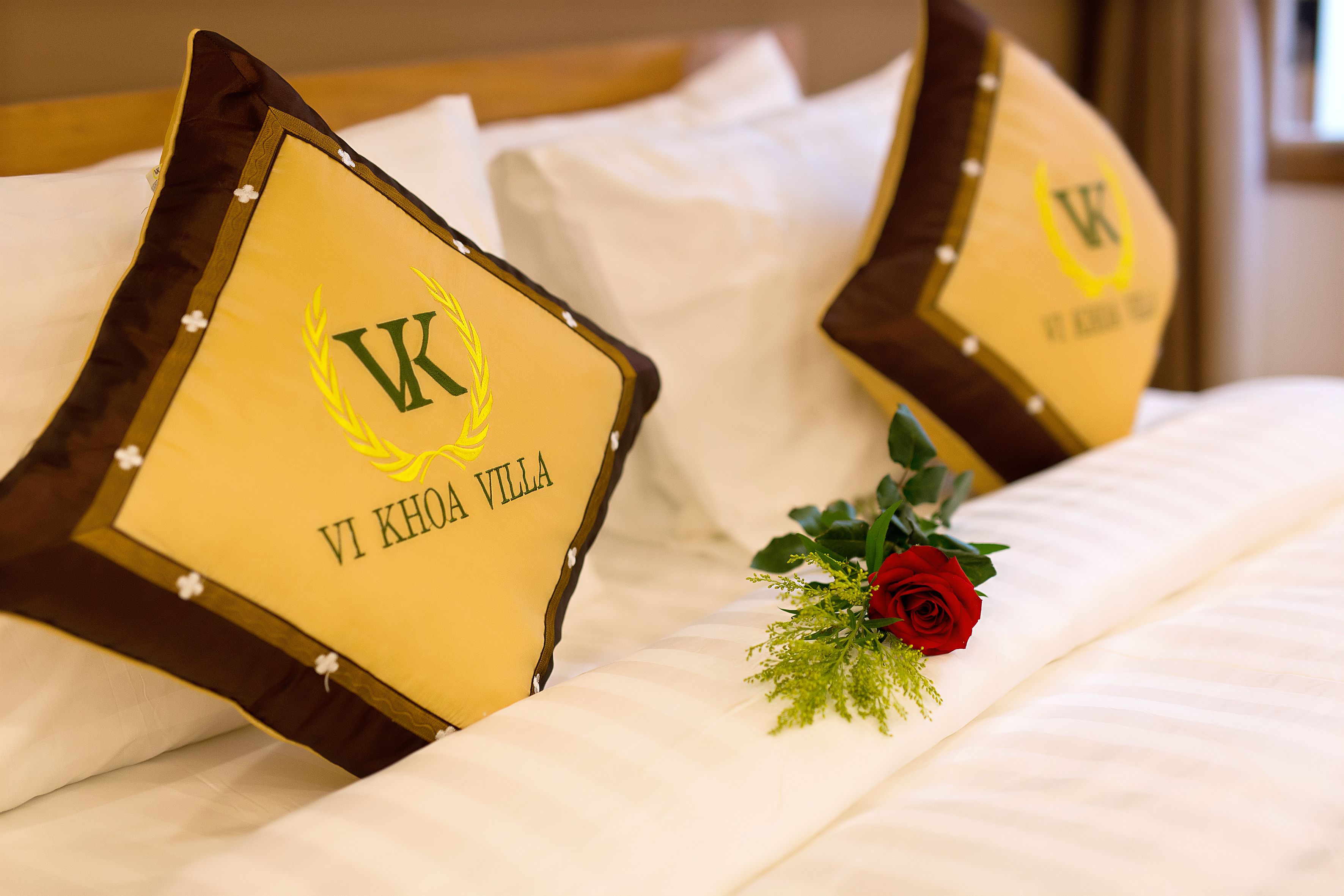 A bed with pillows that have a logo and text, and a red rose on the bed.