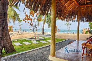 A beachside area with a thatched roof structure, palm trees, and a view of the ocean.