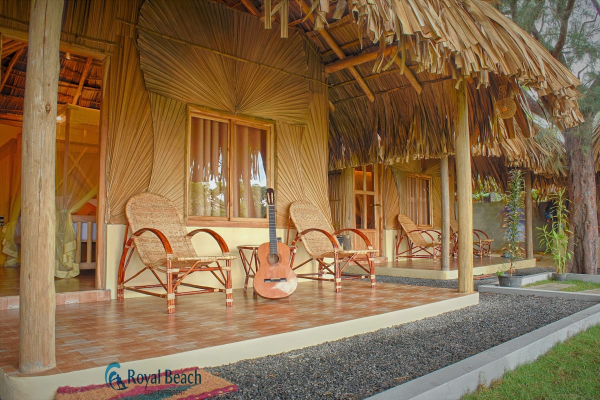 Una estructura con techo de paja, muebles de mimbre y una guitarra, lo que sugiere un ambiente tropical y relajado.