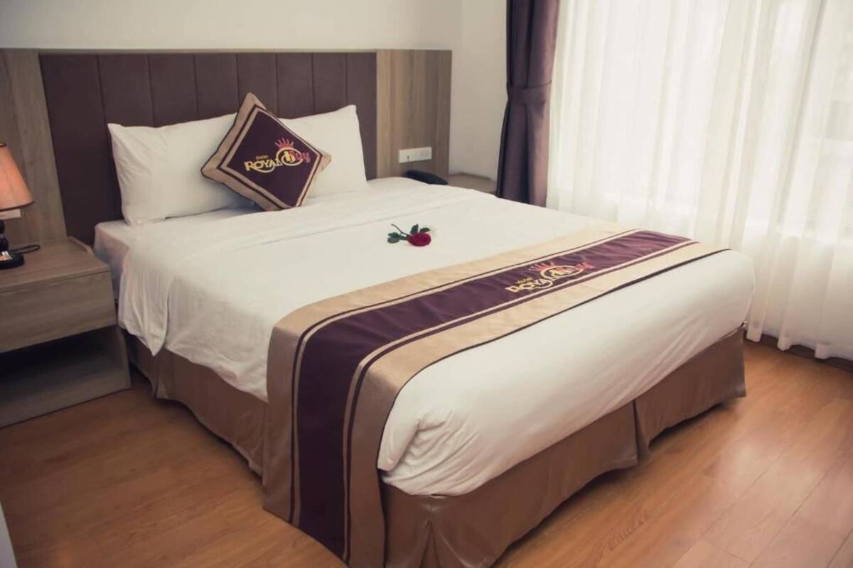 A hotel room with a large bed, a nightstand, a lamp, and a window with curtains.