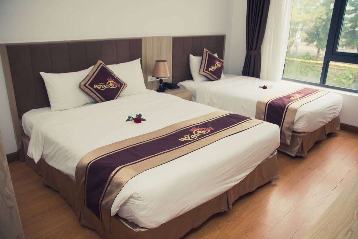 A hotel room with two beds, each with a headboard, a bedside table with a lamp, and a window with curtains.