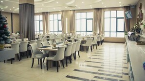 A spacious dining area with multiple tables and chairs, large windows with curtains, and a modern ceiling design.