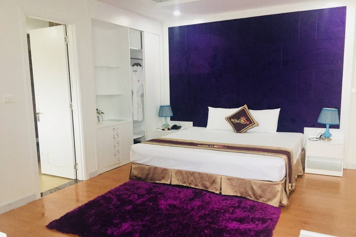 A bedroom with a large bed, a wardrobe, a purple rug, and two bedside lamps.