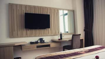 Une chambre d’hôtel comprenant un lit, un bureau avec une chaise, un téléviseur fixé sur un panneau en bois, un miroir et une fenêtre avec des rideaux.