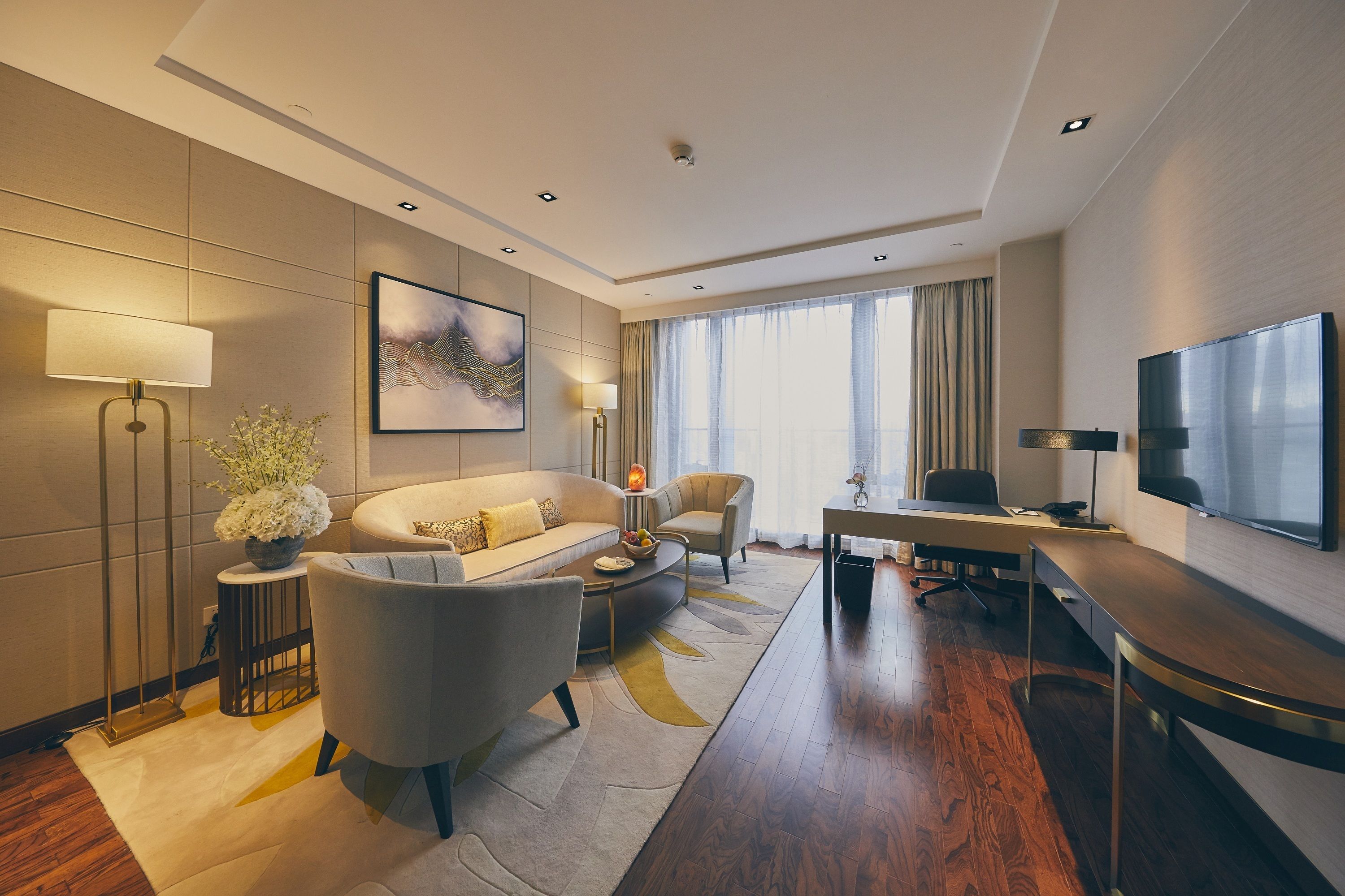 Una habitación de hotel moderna con sofá, sillón, escritorio y televisión.