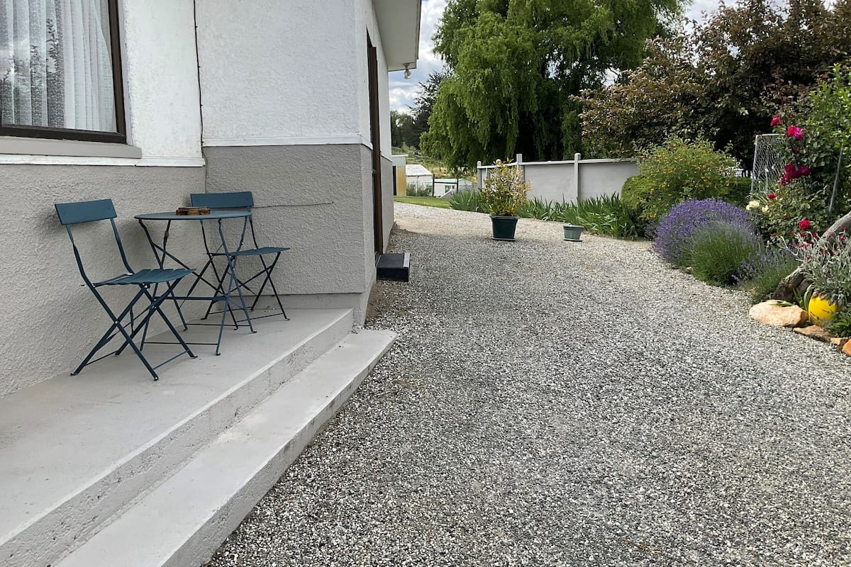 A building with a gravel pathway leading to a seating area with two chairs and a table.
