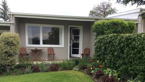 A house with a front yard, two wooden chairs, a small table, and a variety of plants and flowers. - Alexandra Garden Court Motel (Alexandra)
