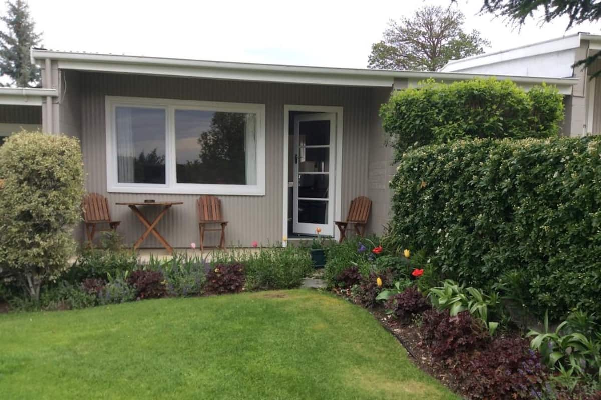 A house with a front yard, two wooden chairs, a small table, and a variety of plants and flowers.
