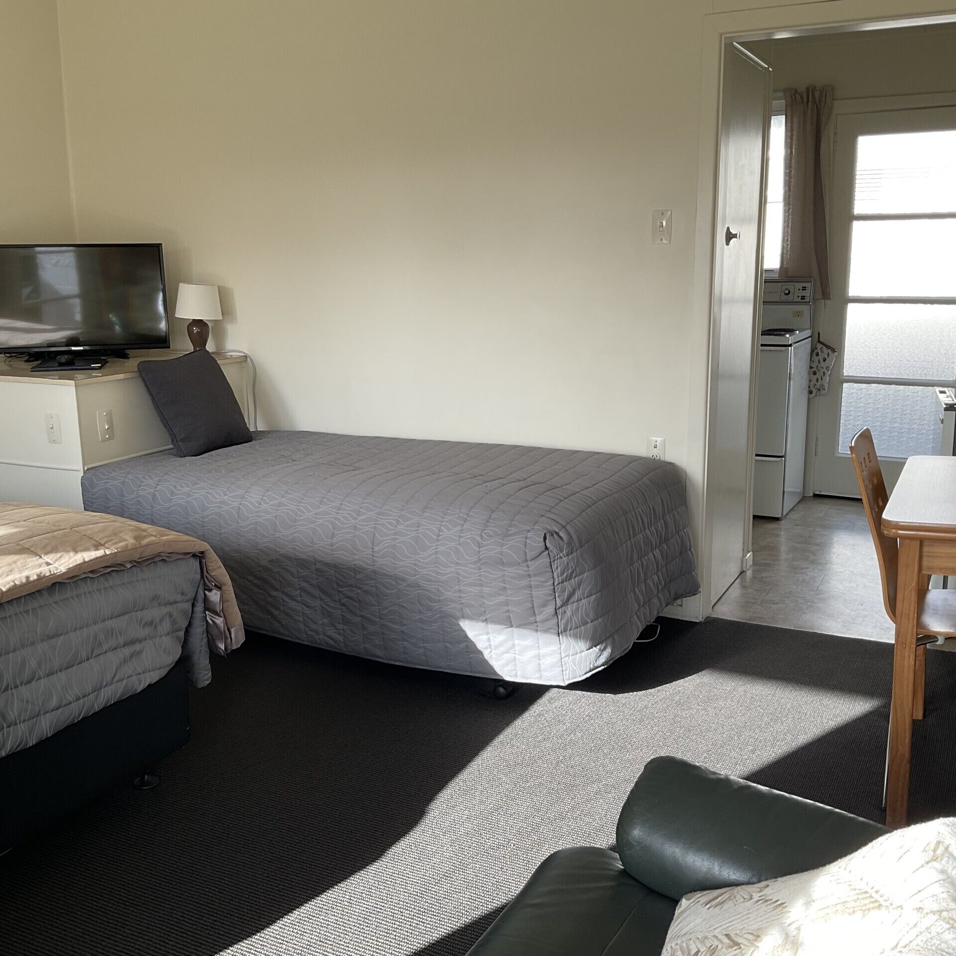 A hotel room with a bed, a TV, a desk, and a kitchenette.