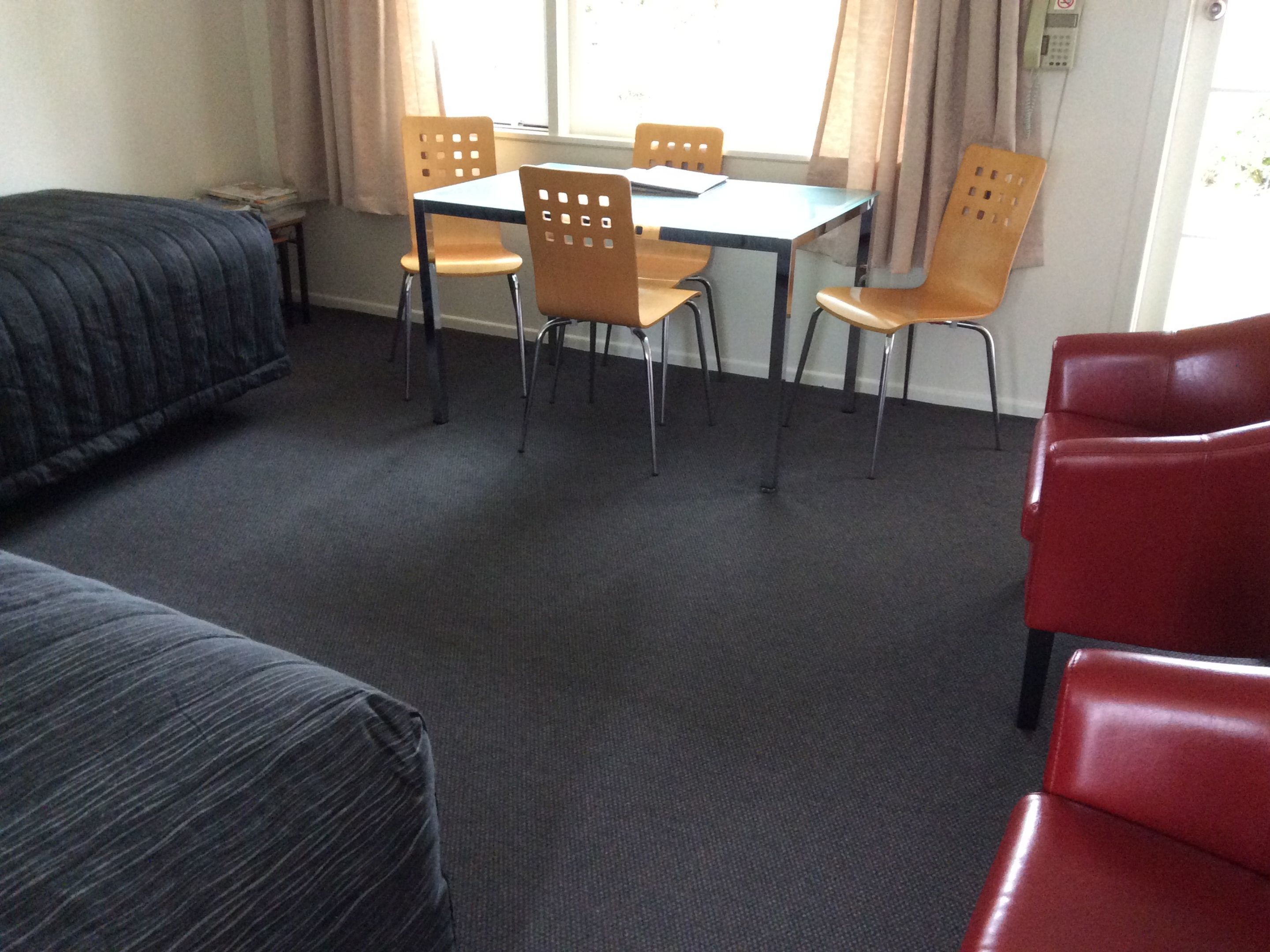 A room with a bed, a table with chairs, and a red chair.