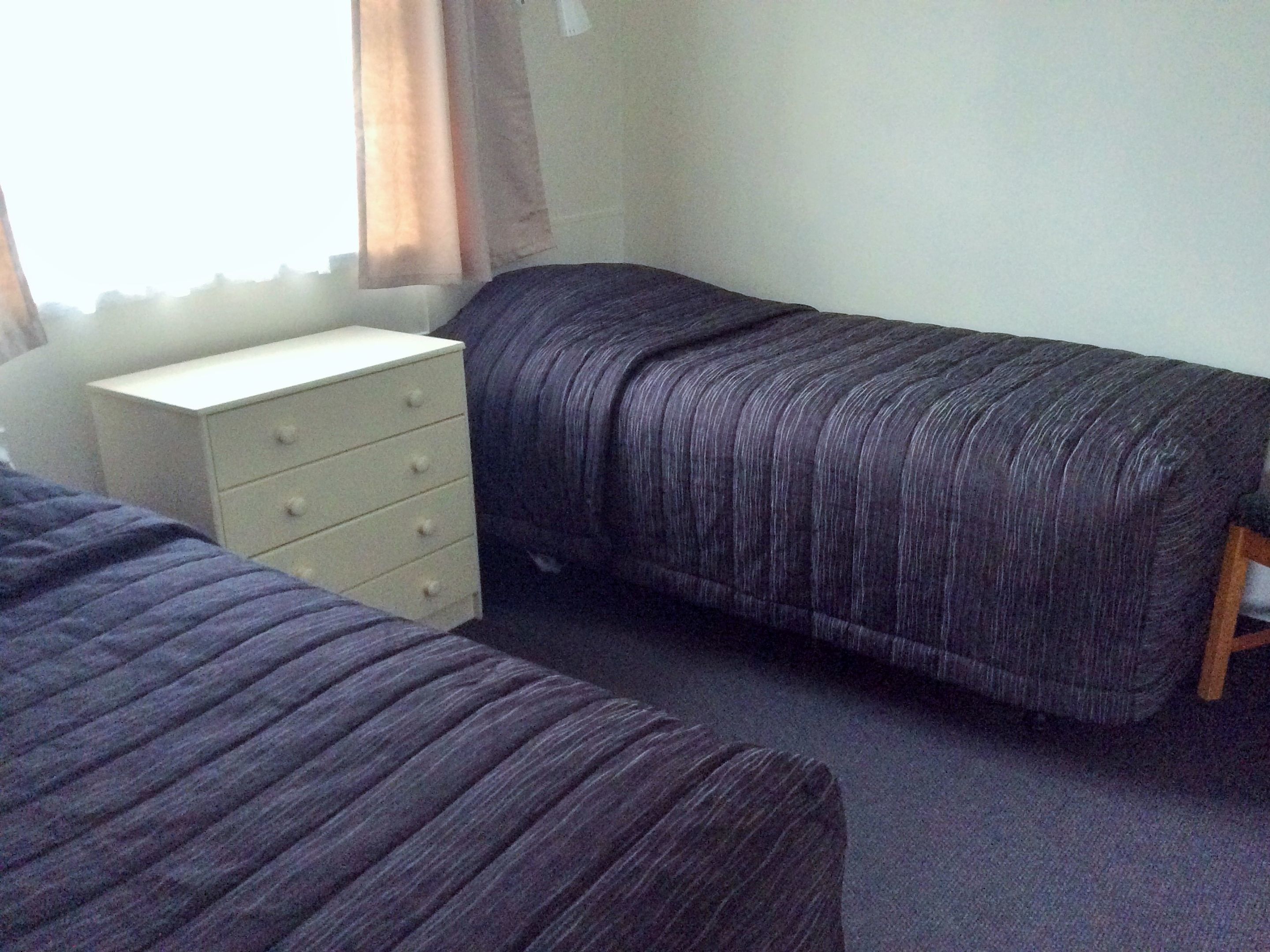 Une chambre avec deux lits, une commode et une fenêtre avec des rideaux.