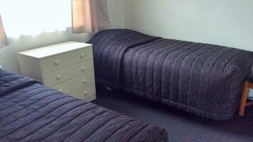Une chambre avec deux lits, une commode et une fenêtre avec des rideaux.