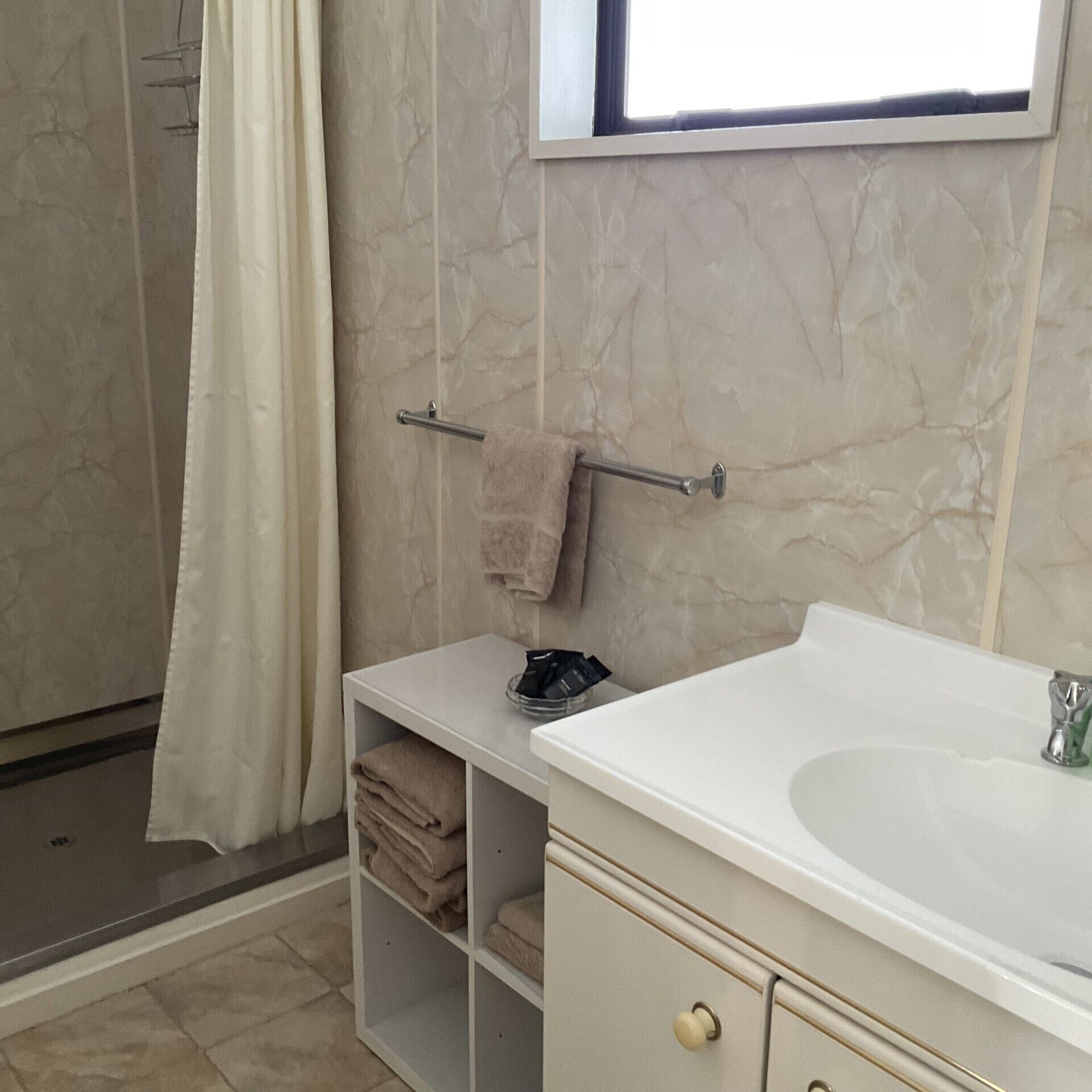 Ein Badezimmer mit weißem Waschbecken, Handtuchhalter, Duschvorhang und Fenster.