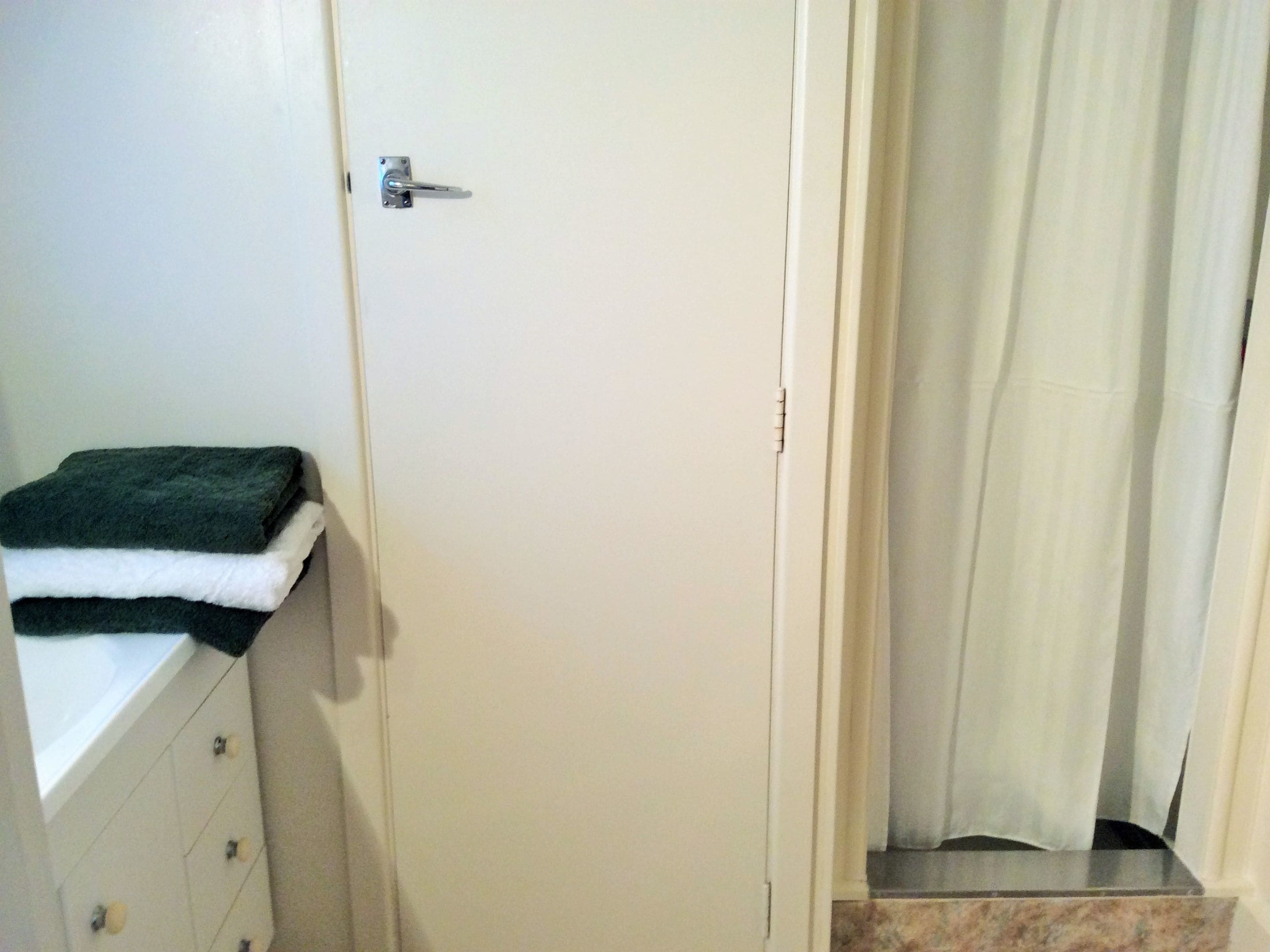 Un baño con una puerta blanca, un perchero con una toalla doblada y una cortina de ducha.