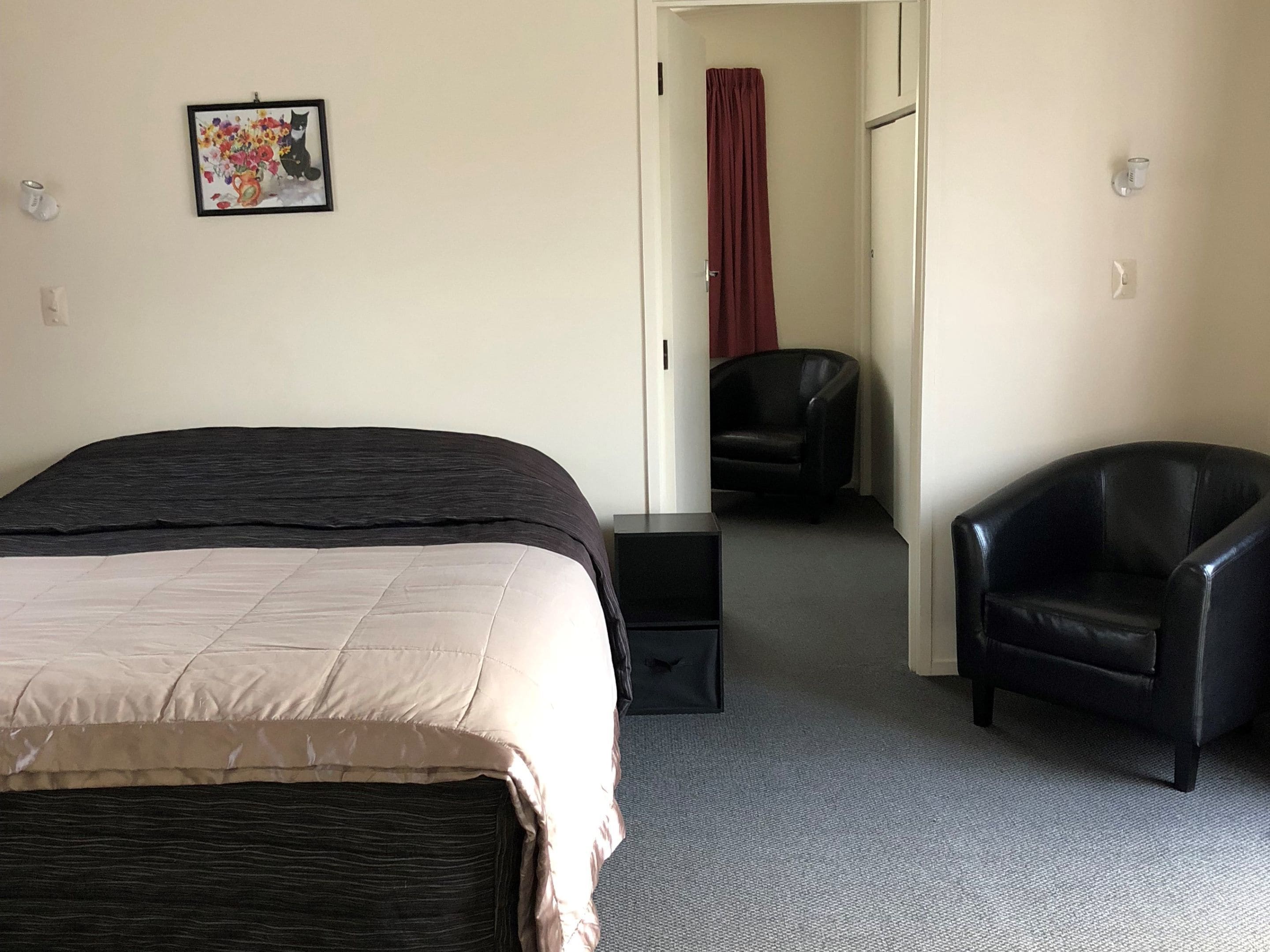 A hotel room with a bed, a chair, a desk, and a door leading to another room.