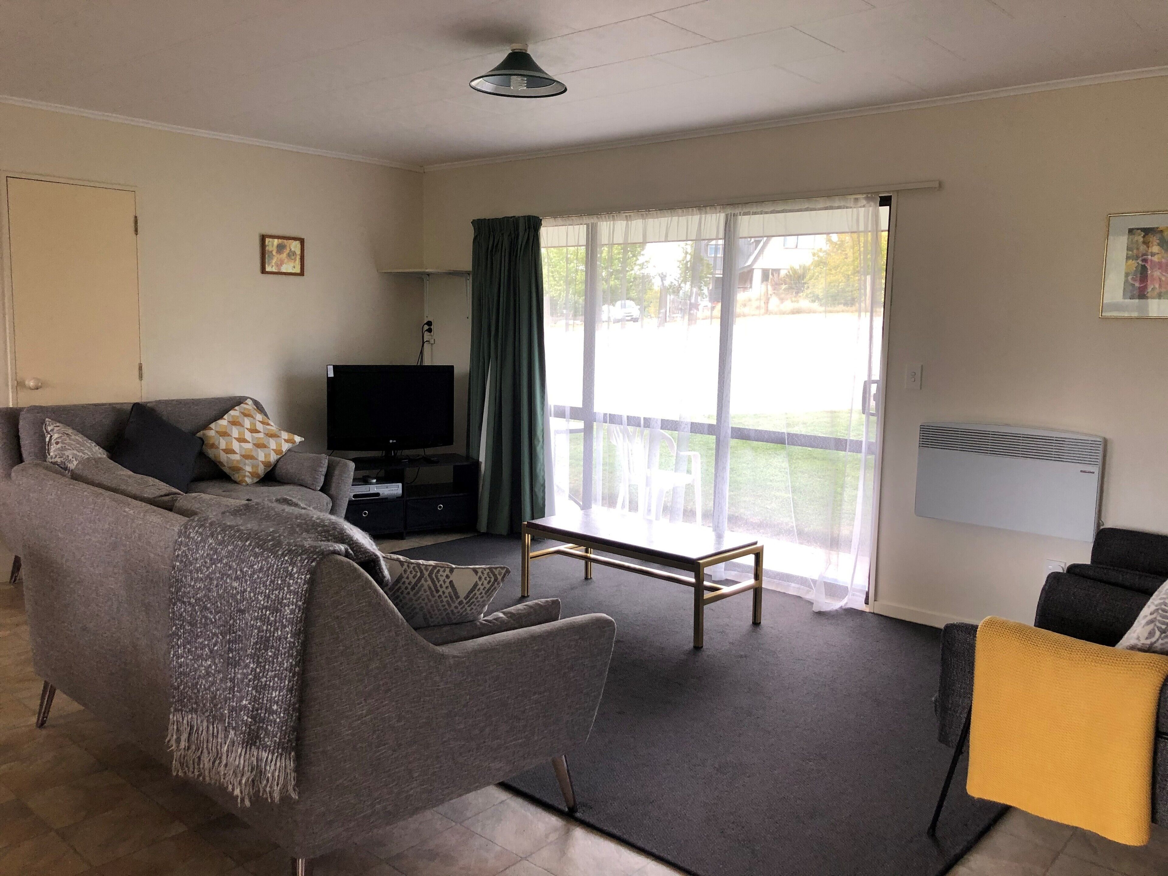 A living room with a sofa, a television, a coffee table, and a chair. There is a sliding glass door leading to an outdoor area.