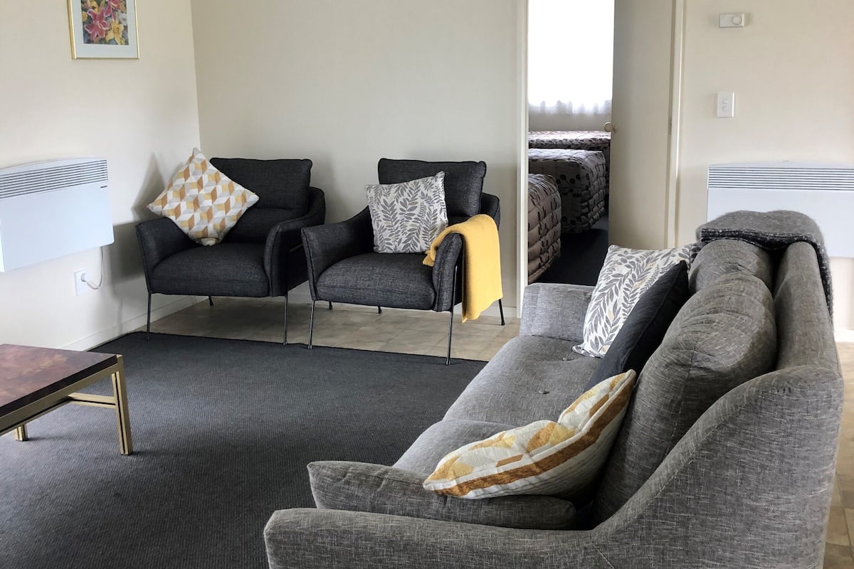 A modern living room with grey sofas, a small table, and a yellow throw blanket.