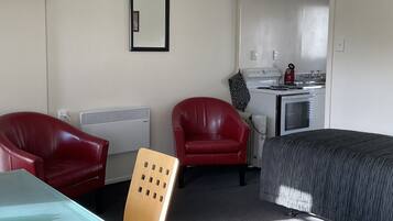 Ein kleines Hotelzimmer mit einem Bett, zwei roten Ledersesseln, einem kleinen Tisch, einer Küchenzeile und einem Spiegel an der Wand.