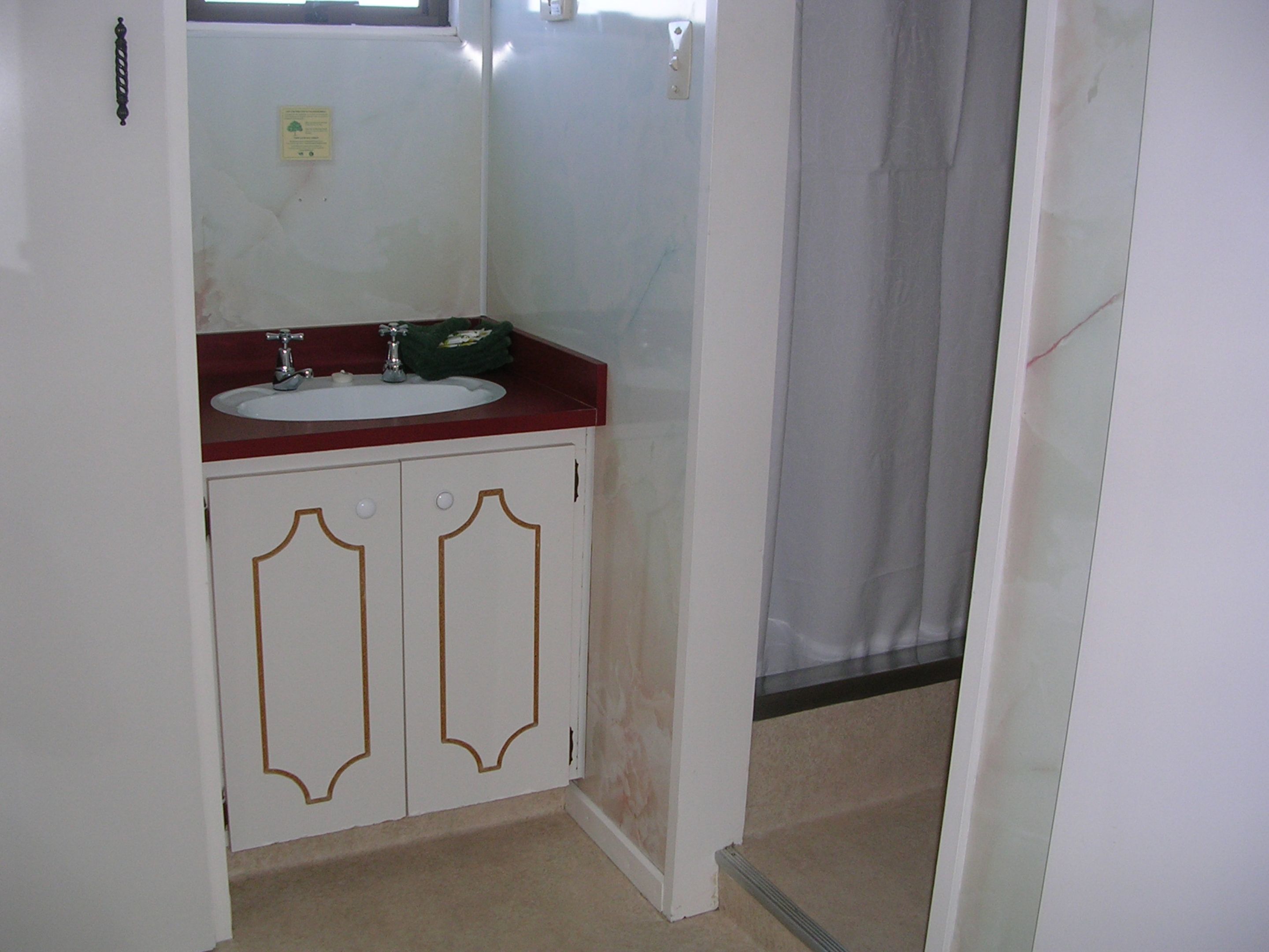 A bathroom with a white sink, red countertop, and two white cabinets with gold trim.