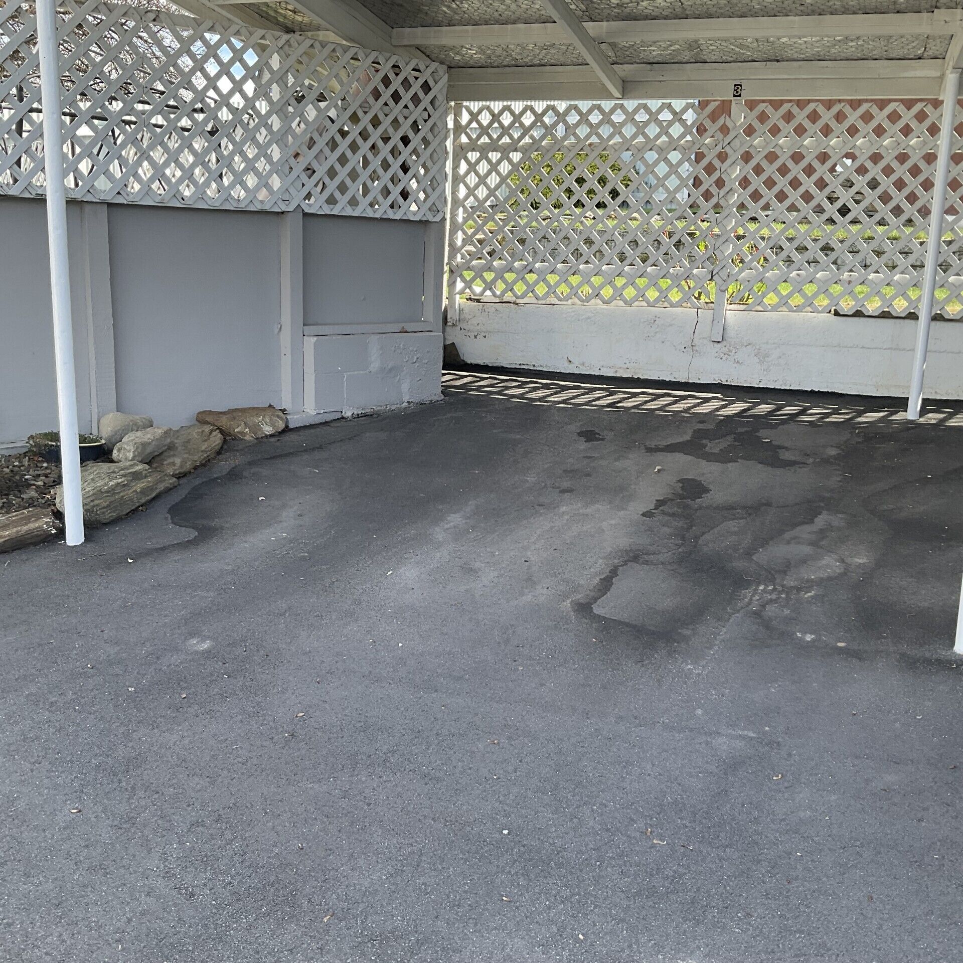 Un espace extérieur abrité, doté d’un sol en béton, d’une clôture en treillis blanc et d’un panneau indiquant le chiffre « 3 ».