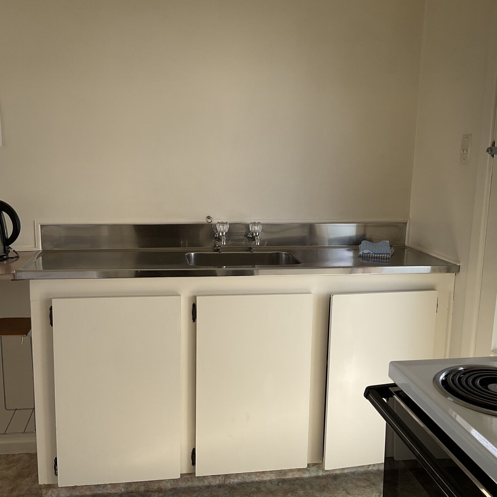 A compact kitchen with a stainless steel sink, a stove, and two white refrigerators.
