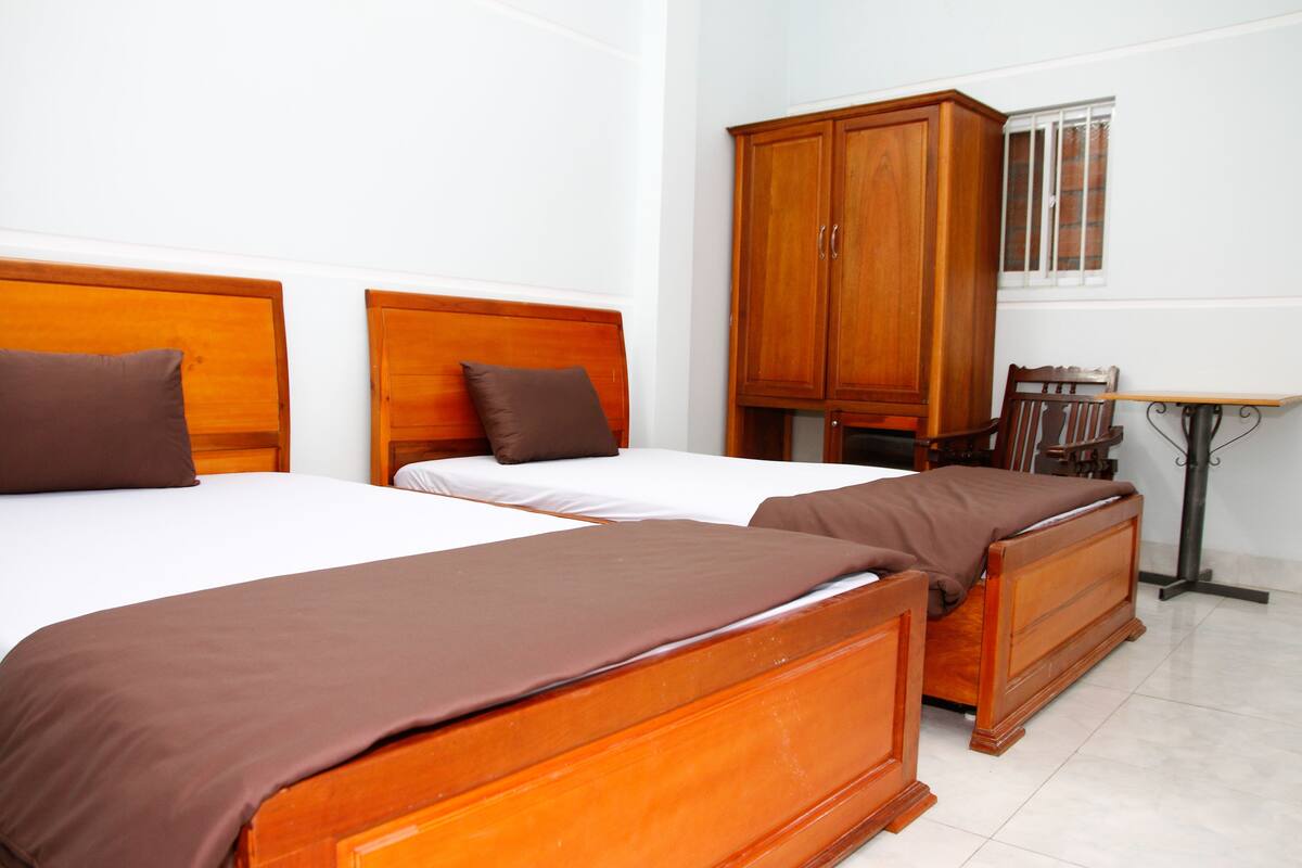 A hotel room with two wooden beds, a wardrobe, a small table, and a window.