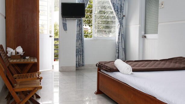 Una habitación con una cama, sillas de madera, un televisor y un ventanal con cortinas.