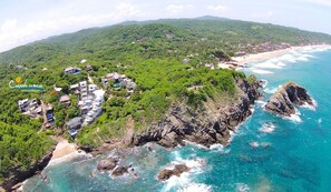 Vue aérienne d’une station balnéaire comprenant plusieurs bâtiments, une plage et des falaises rocheuses.