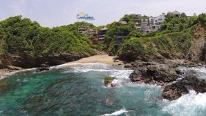 Vista costera con playa, costa rocosa y edificios en una ladera.
