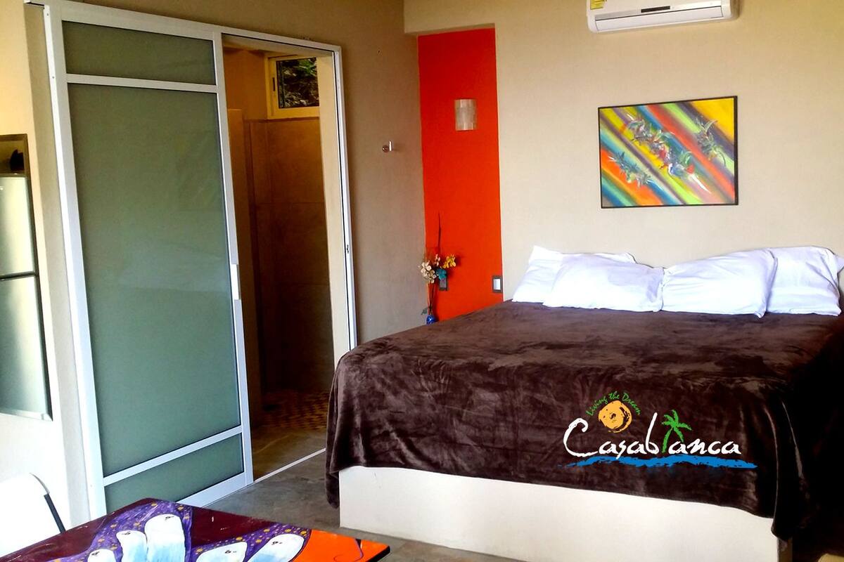 A hotel room with a bed, a sliding door, a colorful artwork on the wall, and a logo on the bedspread.