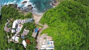 Vista aérea de una propiedad costera con varias edificaciones, una playa y abundante vegetación.