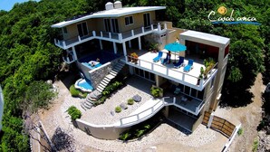 Una casa de dos pisos con piscina, mobiliario exterior y una escalera que conduce al nivel superior.