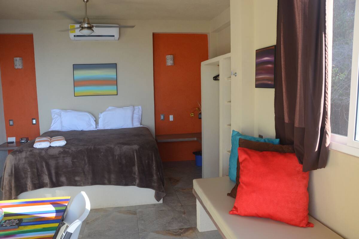 A bedroom with a bed, a desk, a chair, a bench, and a window with curtains.