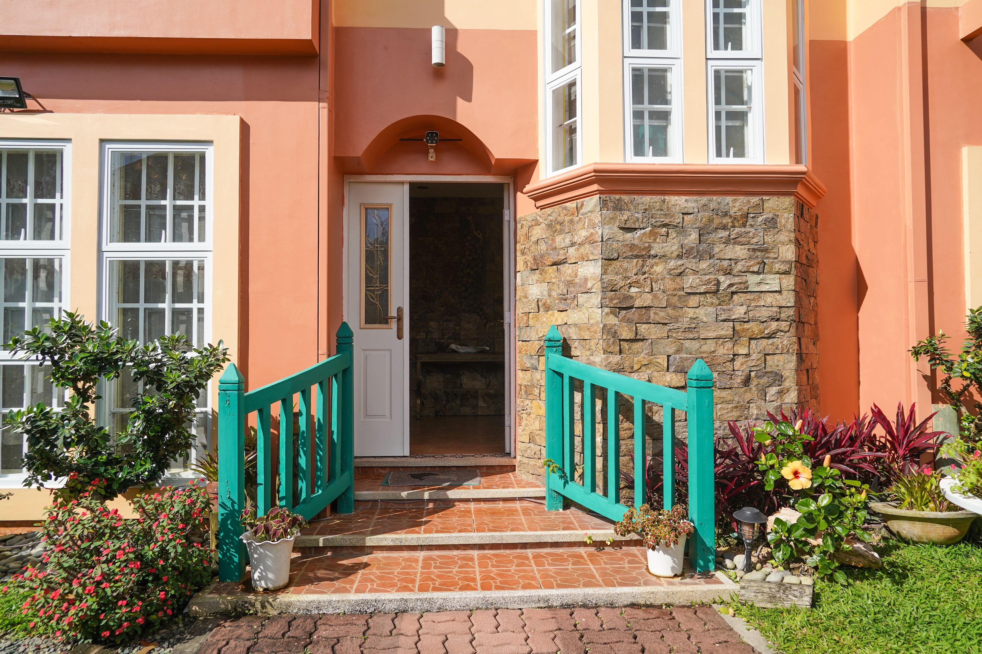 A building entrance with a stone facade, a white door, and a small garden with potted plants and a pathway.