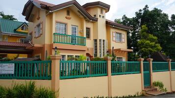 A two-story house with a green fence, a balcony, and a sign indicating it is for rent.