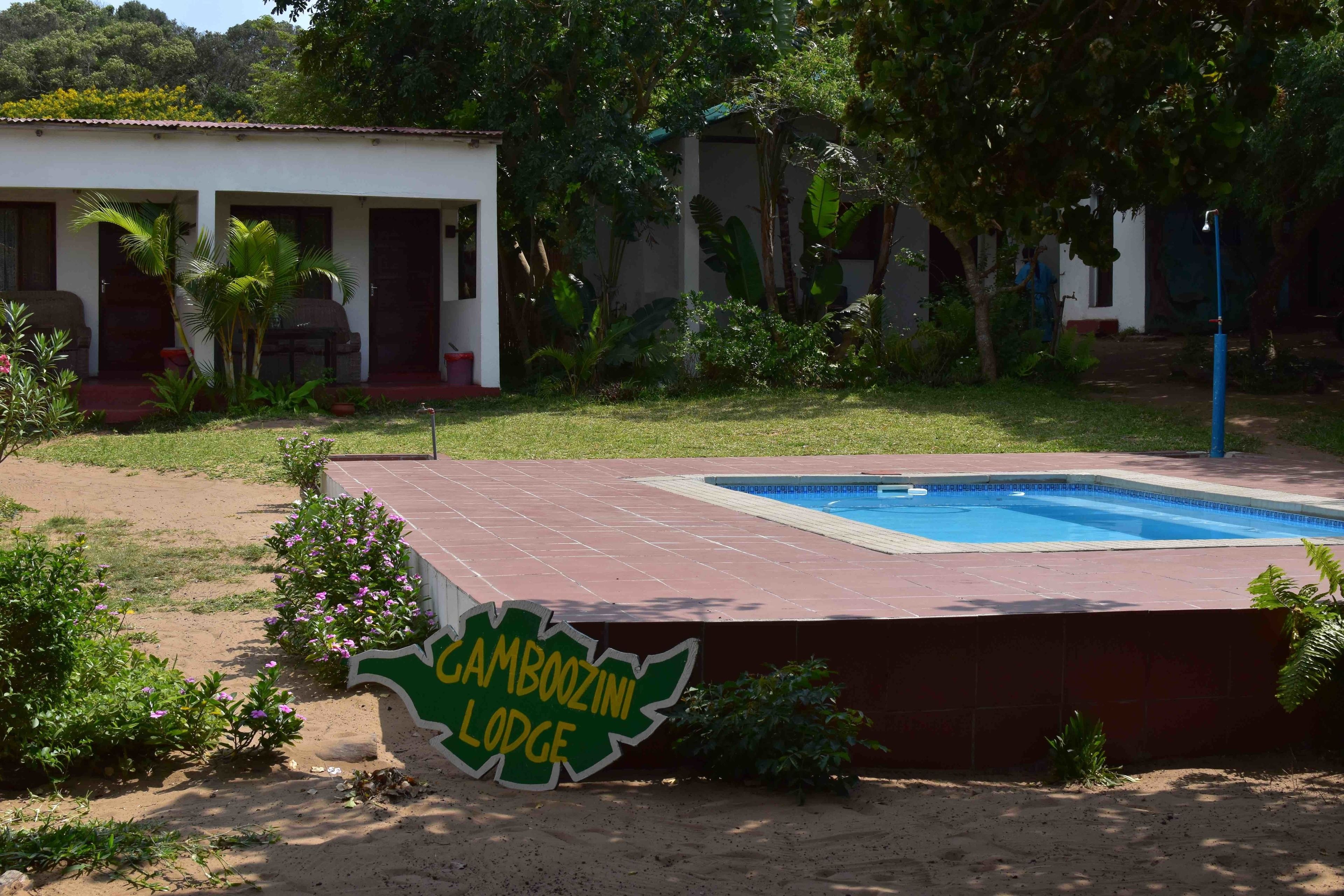 A pool area with a sign reading "Camboozini Lodge" and a building with multiple doors and windows.